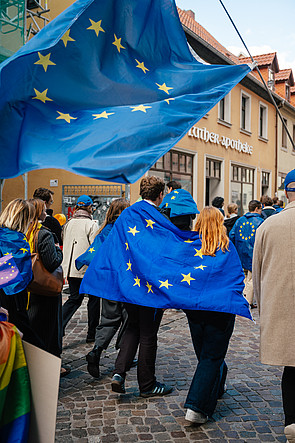 Teilnehmerinnen und Teilnehmer ein Demonstration im Rahmen des JEF-Bundeskongresses. Zwei Personen hüllen sich gemeinsam in eine EU-Flagge. Über beiden wird eine noch größere EU-Flagge geschwenkt.